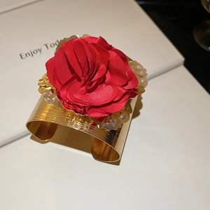 Macro shot of gold bracelet featuring red fabric flowers and pearl accents on book