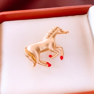 Detail of a matte gold horse brooch with red enamel hooves on white silk lining