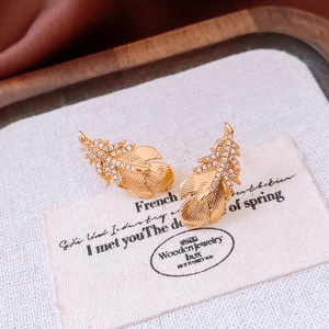 Detail of 18k gold plated feather earrings with micro-inlaid clear zircons on wood