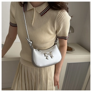 Close-up of silver underarm bag with metal bow detail on a beige polo shirt