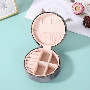 Detailed interior of a round grey velvet jewelry box with pink compartments and ring slots