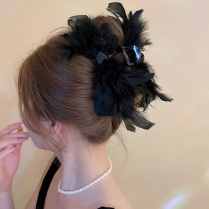 Detail view of a black acrylic claw clip with fluffy feathers and ribbons on dark hair