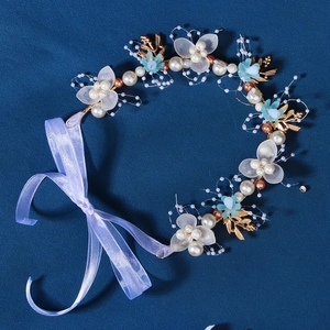 Handmade bridal headband with white flowers, gold leaves, and pearls on a blue background