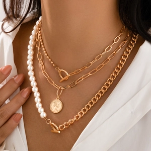 Close-up of layered gold necklace with faux pearls, coin pendant, and toggle clasp detail