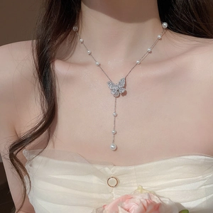Detail of silver pearl necklace with sparkling butterfly pendant and tassels on model