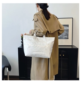 Close-up of pearl white DuPont paper tote bag with textured finish on a camel trench coat