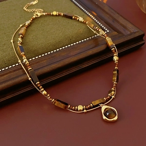 Dettaglio di perline in occhio di tigre e ciondolo a goccia su collana a strati