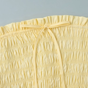 Detail of light yellow smocked fabric and small bow decoration on a vacation set