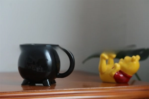Macro shot of high-gloss black ceramic witch cauldron mug on a wooden tabletop