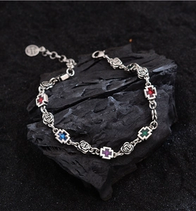 Macro detail of retro silver bracelet featuring rose links and cross charms with colorful gems