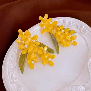 Detailed macro view of yellow resin osmanthus earrings with sparkling green leaves