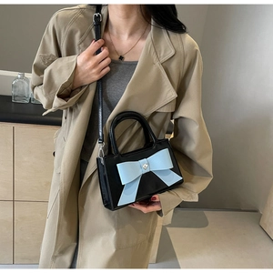 Close-up of a black crossbody bag with a blue bow and heart metal detail on a model
