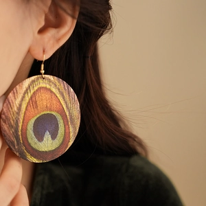 Close-up of bohemian round peacock feather pattern earrings on a model's ear