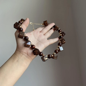 Detail of beaded necklace with leopard print cubes and dark brown beads held in hand