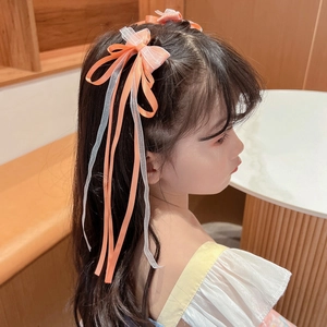 Close-up of a girl wearing orange and white ribbon bow hair clips with tassels