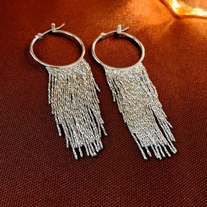 Detailed close-up of silver hoop earrings with long metallic tassels on textured fabric