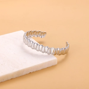Close-up of a silver-toned open bangle with vintage ribbed texture on a white stone base