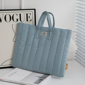 Detail of light blue quilted laptop bag with vertical stitching and woven label