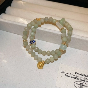 Detail of light green beaded double-layer bracelet with gold bell and blue enamel cloud charms
