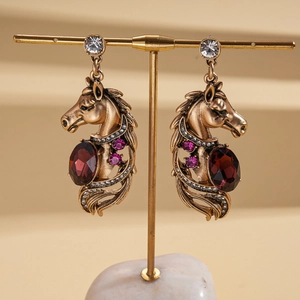 Vintage gold horse-head earrings with red gemstones and crystals on a display stand
