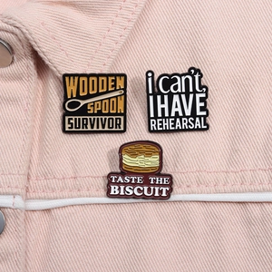 Close-up of three metal enamel pins with phrases on a pink denim jacket