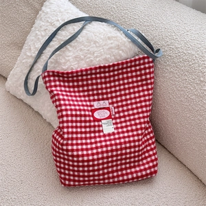 Close-up of red plaid canvas tote bag with blue denim strap on a soft beige sofa