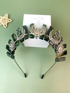 Detailed close-up of green raw stone crown with silver moon and snake charms