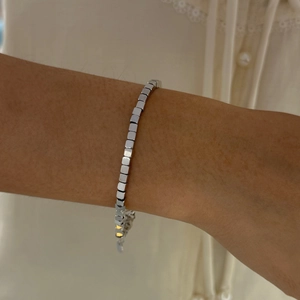 Detail of silver stainless steel cube link bracelet worn by a model on soft fabric