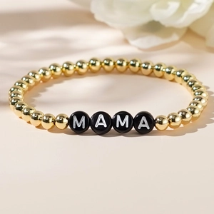 Close-up of golden beaded MAMA bracelet with letter charms on a warm background
