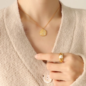Golden shell pearl necklace and ring set shown on a model with beige knitwear background