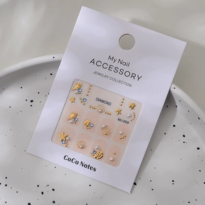 Macro detail of MJ-009 nail art set with gold shells, stars, and pearls on white card