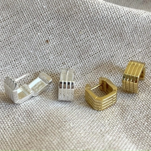 Close-up of gold and silver rectangular hoop earrings with textured parallel stripes