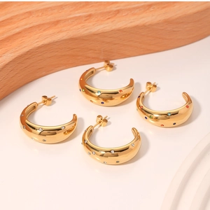 Detail of C-shaped gold-plated earrings with clear cubic zirconia and colorful gemstones