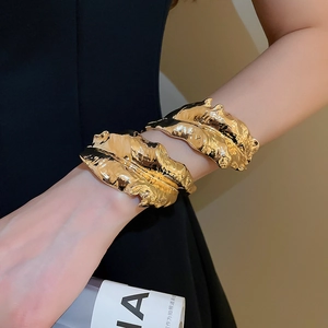 Macro detail of glossy golden crumpled leaf textured bracelets on a model wrist