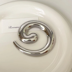 Close-up of a silver spiral stainless steel brooch with a polished mirror finish on a dish
