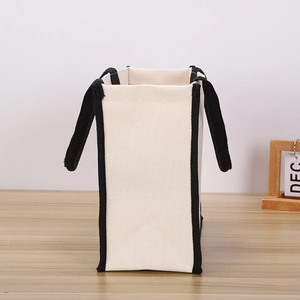 Minimalist beige canvas tote bag with black handles and trim shown in side view