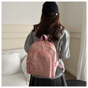 Pink floral embroidered mini backpack detail showing zipper and woven strap on model