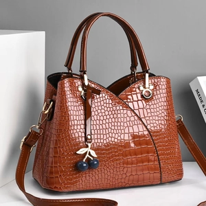 Detail of glossy brown crocodile pattern PU leather tote with a decorative cherry charm