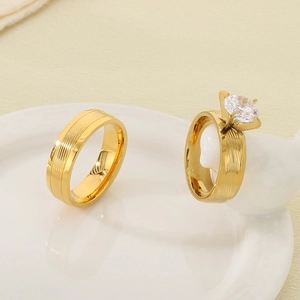 Detail of gold engagement ring with round zircon and brushed metal band on ceramic tray