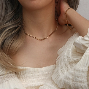 Close-up of a model wearing a triple-layer gold flat curb chain necklace and bracelet set
