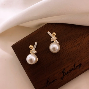 Macro shot of twisted gold metal earrings with pavé zircons and white round pearls