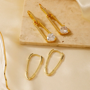 Luxury gold safety pin earrings with sparkling heart-shaped zircon on silk and marble