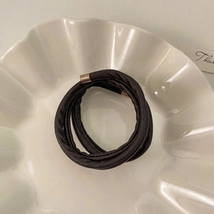 Detail of dark brown leather hair tie with rose gold metal clasp on white ceramic tray
