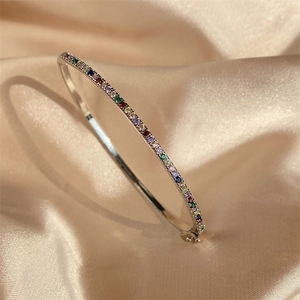 Macro detail of silver bangle with pavé rainbow gemstones on champagne silk