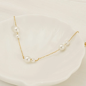 18K gold stainless steel chain necklace with alternating pearls in a white shell dish