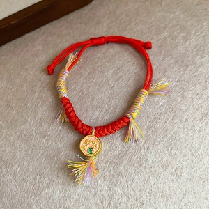 Gros plan d'un bracelet en corde tressée rouge avec pendentif doré et pompon dégradé coloré