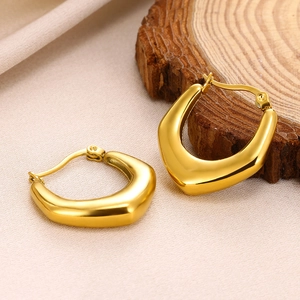 Macro shot of gold geometric U-shaped earrings on elegant satin and wood background