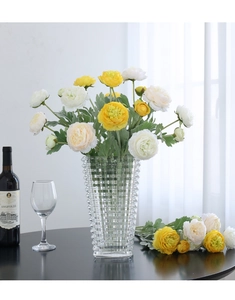 Close-up of yellow and white faux peonies in a diamond-textured glass vase