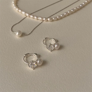 Detail showing elegant silver earrings with zircon and pearls on textured beige paper