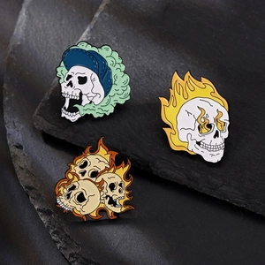 Trois pin's punk gothique en émail avec crânes et flammes sur une surface rocheuse
